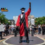 photo of Black man in academic regalia in the center of a Black Lives Matter assembly
